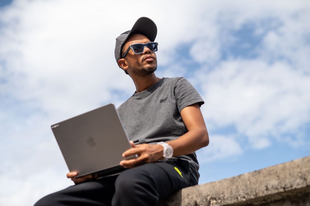 Me wearing sunglasses holds a laptop while gazing thoughtfully toward the horizon, with a dramatic cloudy sky unfolding in the background.